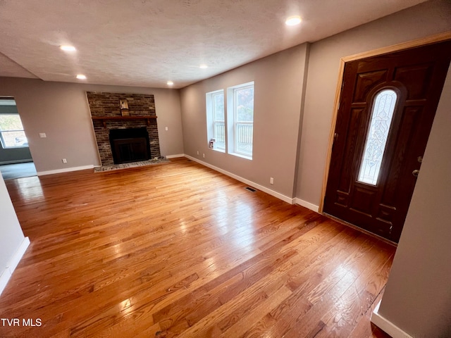 unfurnished living room featuring a fireplace, a textured ceiling, and light hardwood / wood-style flooring