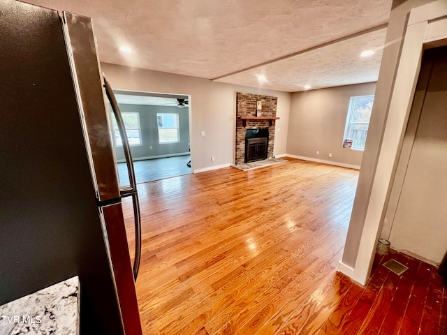 unfurnished living room with a textured ceiling, hardwood / wood-style flooring, a brick fireplace, and ceiling fan