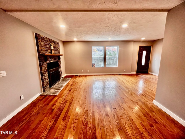 unfurnished living room with wood-type flooring, a textured ceiling, and a brick fireplace