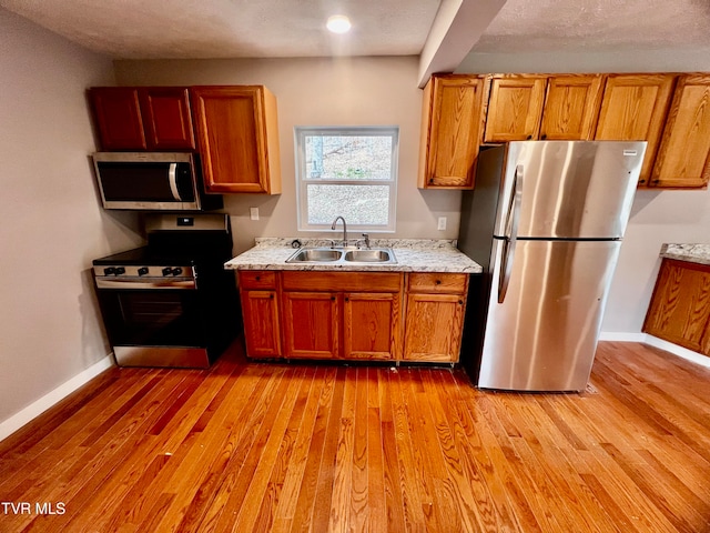 kitchen featuring a textured ceiling, sink, stainless steel appliances, and light hardwood / wood-style flooring