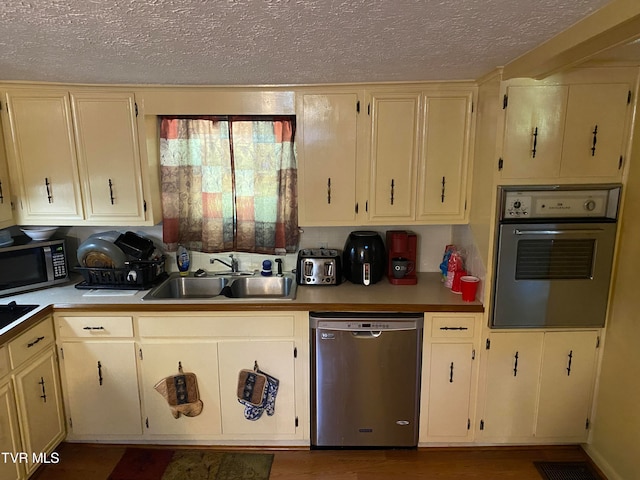 kitchen featuring hardwood / wood-style floors, cream cabinets, a textured ceiling, sink, and stainless steel appliances