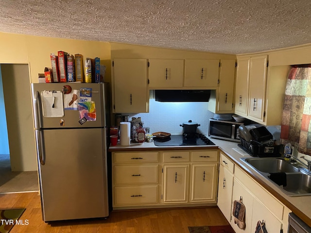 kitchen with appliances with stainless steel finishes, cream cabinets, range hood, and light hardwood / wood-style floors