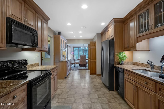 kitchen with sink, an inviting chandelier, light stone counters, and black appliances