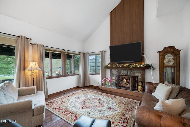 living room featuring wood-type flooring, high vaulted ceiling, and a stone fireplace