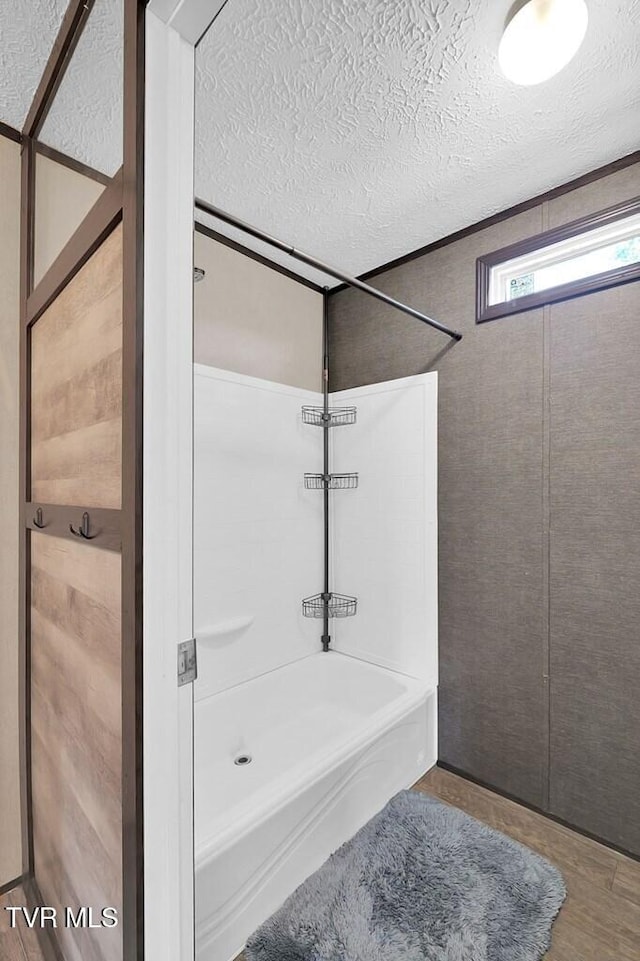 full bathroom with a textured ceiling, bathing tub / shower combination, and wood finished floors