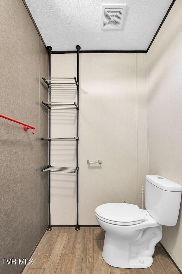 bathroom featuring ornamental molding, a textured ceiling, hardwood / wood-style flooring, and toilet