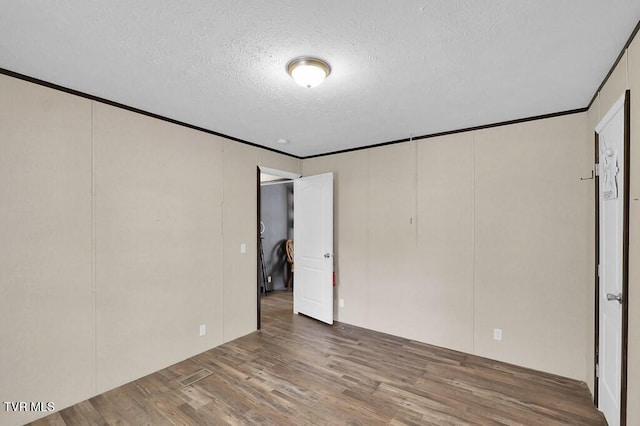 unfurnished bedroom featuring a textured ceiling, ornamental molding, wood finished floors, and a decorative wall
