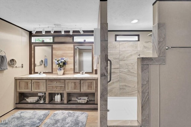 bathroom with track lighting, a textured ceiling, ornamental molding, a shower with shower door, and vanity