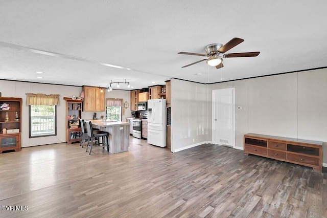 kitchen featuring a kitchen island, dark hardwood / wood-style flooring, ceiling fan, stainless steel appliances, and a breakfast bar