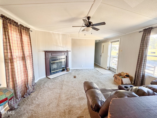 carpeted living room with a textured ceiling, ceiling fan, a tiled fireplace, and wood walls