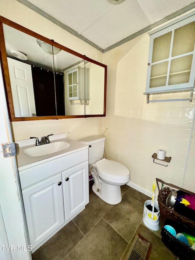 bathroom with toilet, vanity, tile patterned floors, and tile walls