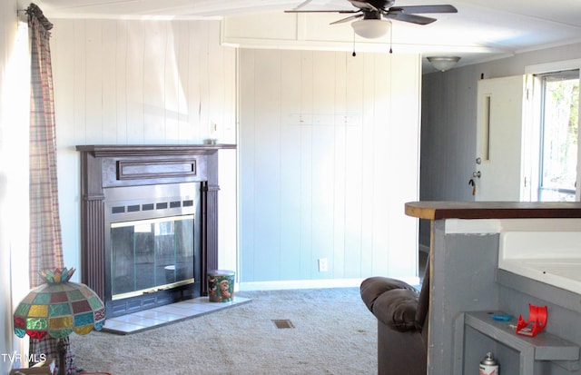 carpeted living room with ceiling fan, crown molding, and wooden walls