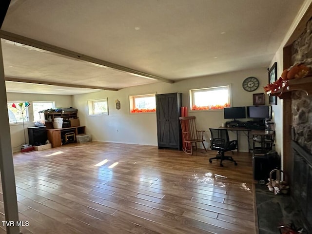 office area featuring a stone fireplace, hardwood / wood-style floors, beam ceiling, and plenty of natural light