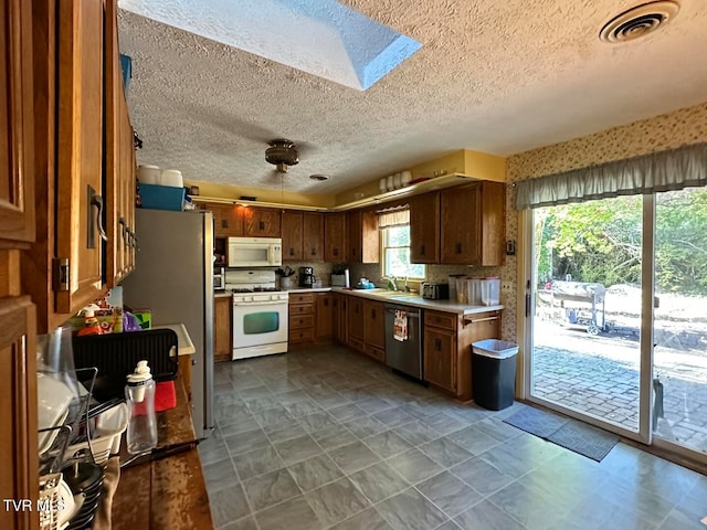 kitchen featuring white appliances, a skylight, sink, a textured ceiling, and decorative backsplash