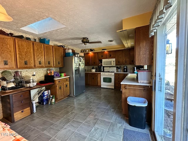 kitchen featuring white appliances, a textured ceiling, a skylight, and decorative backsplash