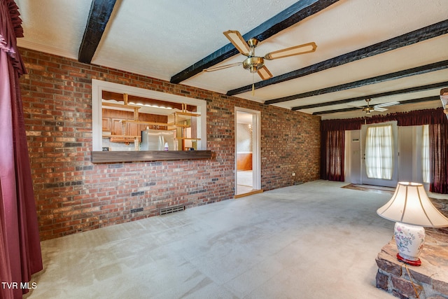 unfurnished living room with beam ceiling, carpet, a textured ceiling, and brick wall