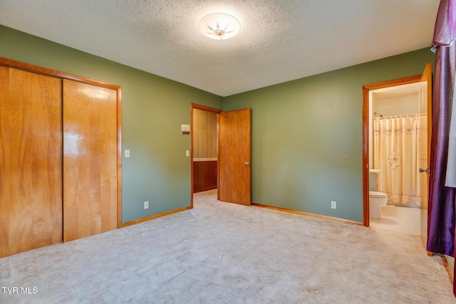 unfurnished bedroom featuring ensuite bath, light colored carpet, a closet, and a textured ceiling