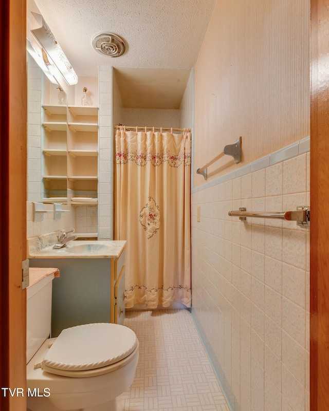 bathroom with tile walls, vanity, a textured ceiling, and toilet