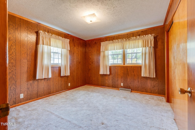 carpeted spare room featuring ornamental molding, a textured ceiling, and wooden walls