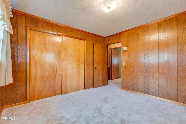 unfurnished bedroom with light colored carpet, a closet, and wood walls