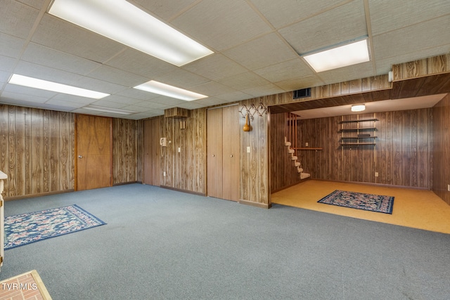 basement featuring light carpet, a drop ceiling, and wood walls