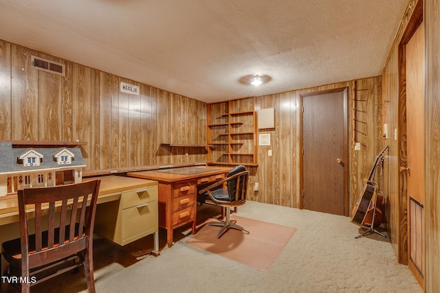 carpeted office featuring built in desk, wooden walls, and a textured ceiling