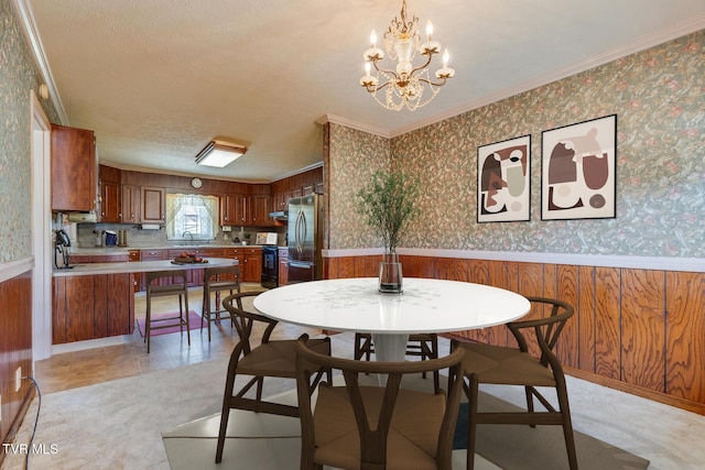 dining space featuring sink, wood walls, a textured ceiling, ornamental molding, and a notable chandelier