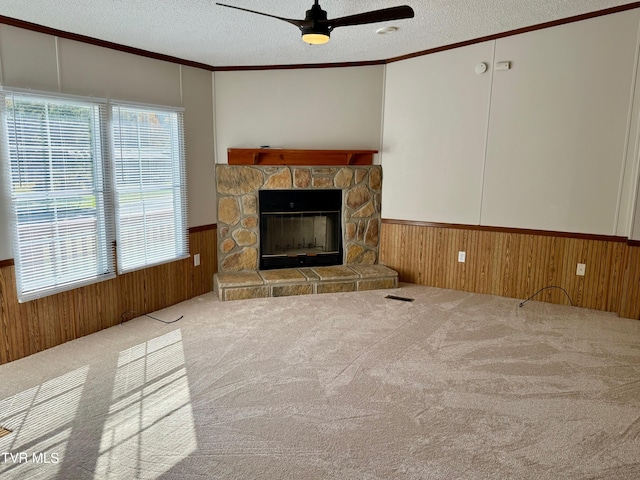 unfurnished living room with a stone fireplace, a textured ceiling, ornamental molding, ceiling fan, and carpet