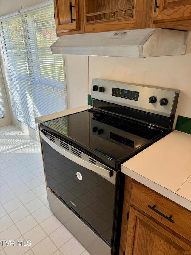 4527 Dorchester Rd, Norton, VA 24273 - kitchen with stainless steel range with electric stovetop, brown cabinets, under cabinet range hood, light tile patterned floors, and light countertops