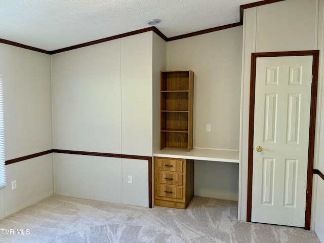 unfurnished office featuring built in desk, light carpet, crown molding, and a textured ceiling