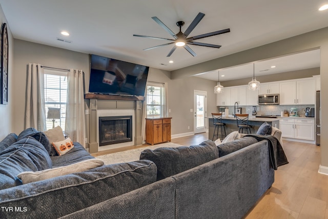 living room with a wealth of natural light, light hardwood / wood-style flooring, and ceiling fan