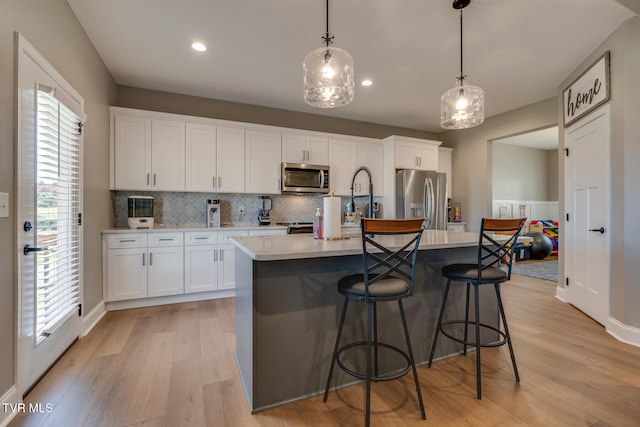 kitchen with appliances with stainless steel finishes, white cabinets, decorative light fixtures, and an island with sink