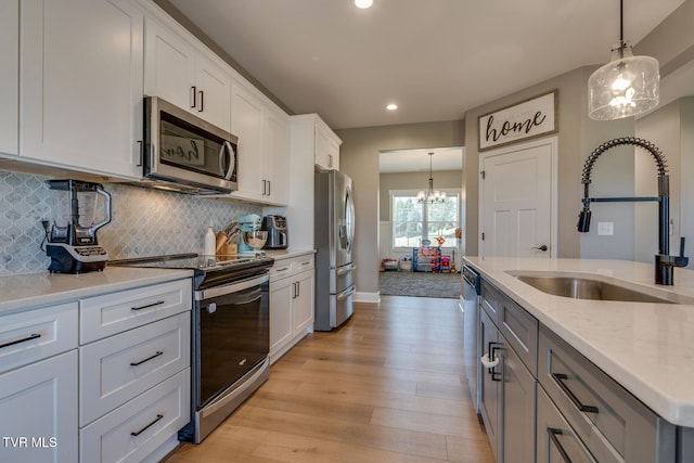 kitchen featuring white cabinets, appliances with stainless steel finishes, light hardwood / wood-style flooring, pendant lighting, and sink