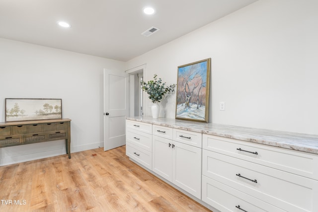 interior space with light hardwood / wood-style floors, light stone countertops, and white cabinets