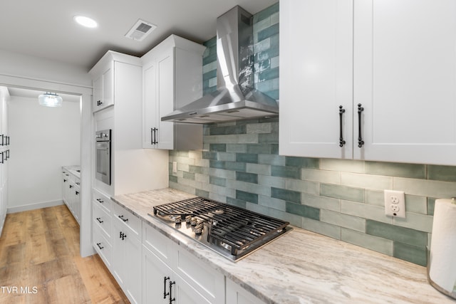 kitchen featuring tasteful backsplash, white cabinetry, stainless steel appliances, wall chimney exhaust hood, and light hardwood / wood-style flooring