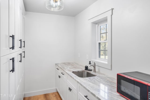 kitchen with sink, white cabinets, light stone counters, and light hardwood / wood-style flooring