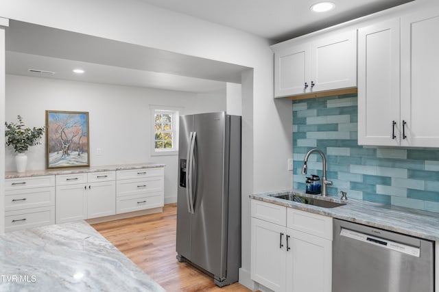 kitchen featuring white cabinets, tasteful backsplash, appliances with stainless steel finishes, light wood-type flooring, and sink