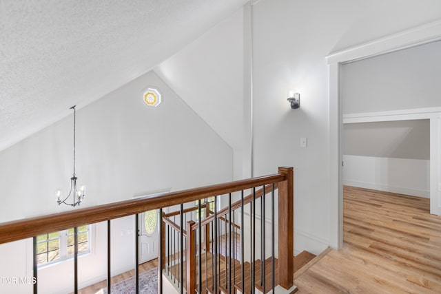 hallway with hardwood / wood-style flooring, a textured ceiling, vaulted ceiling, and an inviting chandelier