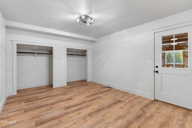 unfurnished bedroom featuring multiple closets and light wood-type flooring