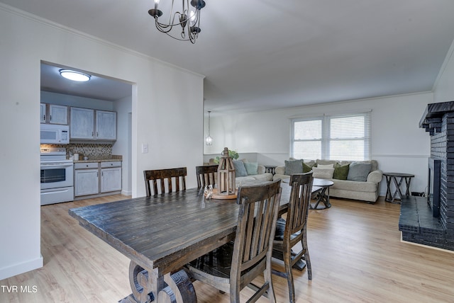 dining area with a notable chandelier, crown molding, light hardwood / wood-style floors, and a brick fireplace