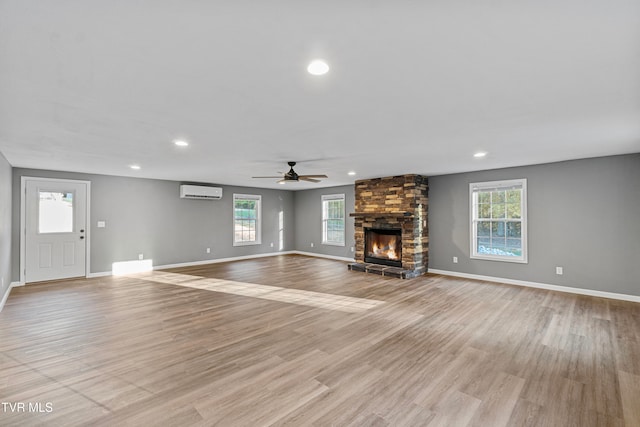 unfurnished living room with a fireplace, a wall mounted air conditioner, ceiling fan, and light hardwood / wood-style floors