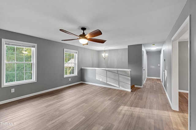 empty room featuring ceiling fan with notable chandelier and light wood-type flooring