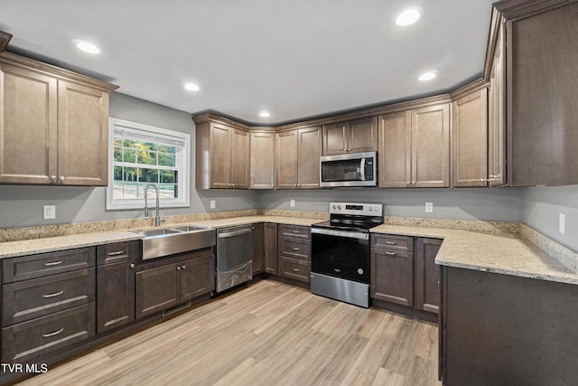 kitchen with a sink, appliances with stainless steel finishes, light wood-style floors, light stone countertops, and recessed lighting