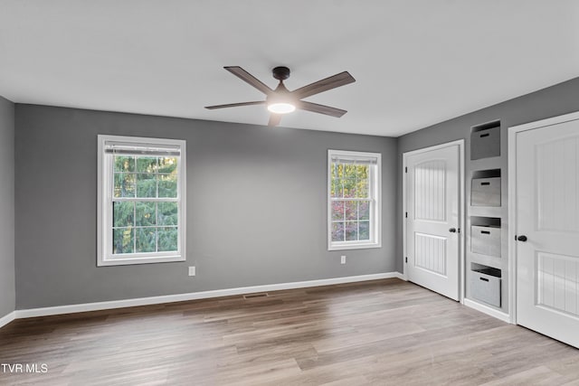 unfurnished bedroom with wood finished floors, multiple windows, and multiple closets