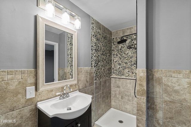 full bathroom with a wainscoted wall, tile walls, tiled shower, and vanity