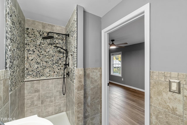 full bath with wood finished floors, a ceiling fan, tiled shower, and tile walls