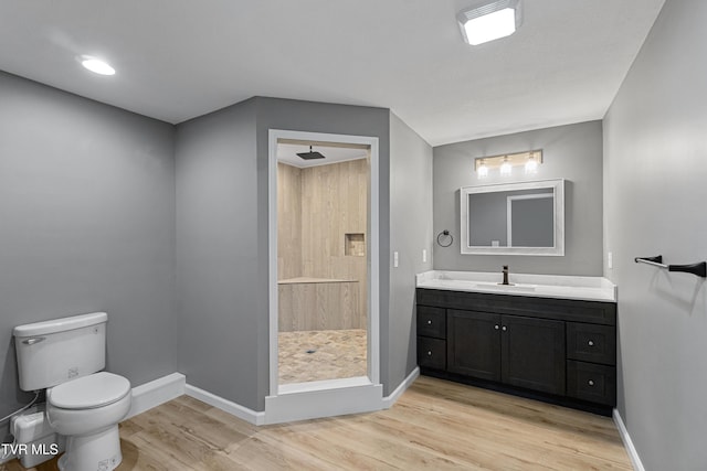 bathroom featuring wood finished floors, toilet, tiled shower, and baseboards