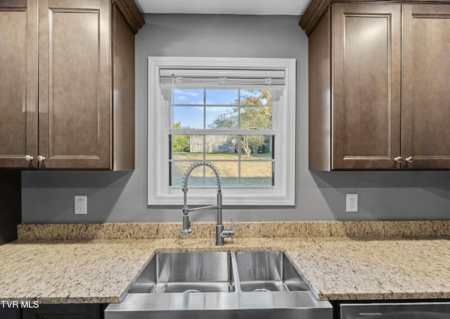 kitchen featuring light stone countertops, dark brown cabinetry, and sink