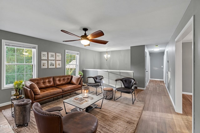 living room with ceiling fan with notable chandelier, wood finished floors, and baseboards