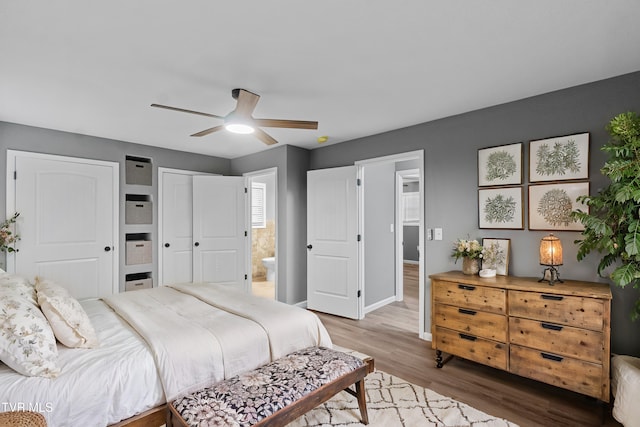 bedroom with connected bathroom, two closets, ceiling fan, baseboards, and wood finished floors
